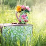 Valise vintage posée dans l'herbe haute avec un vase garni de fleurs